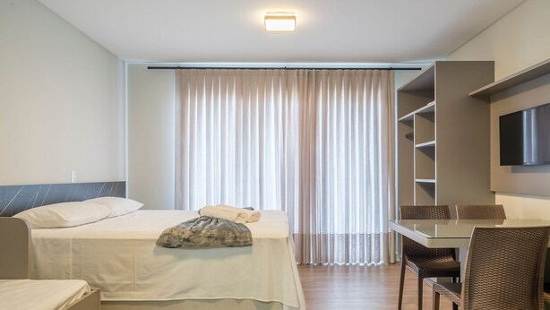 A hotel room with a bed, a desk, and a TV. - VFR Estudios proximos a praia de Bombas (Bombinhas)