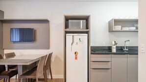 A compact kitchen with a microwave, refrigerator, and a dining area with chairs and a table. - VFR Estudios proximos a praia de Bombas (Bombinhas)