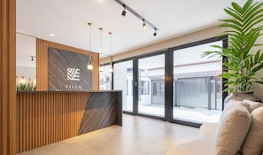 A modern reception area with a marble counter, wooden paneling, and large windows offering a view of the outside. - VFR Estudios proximos a praia de Bombas (Bombinhas)