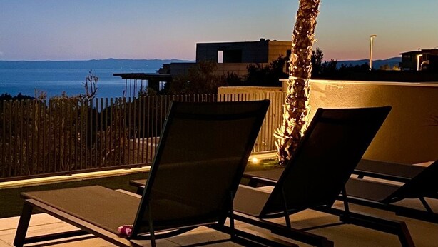 Een terras op het dak met twee loungestoelen, een palmboom en uitzicht op zee.