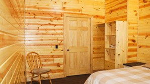 Ein Zimmer in einer Holzhütte mit einem Bett, einem Sessel, einem Kleiderschrank und einer Tür.