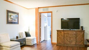 Una sala de estar con un sofá, un televisor sobre un mueble de madera y un cuadro en la pared.