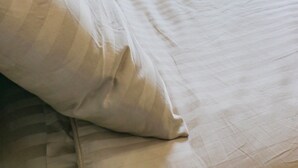 Una cama bien tendida con ropa blanca en una habitación con ventana y cortinas.