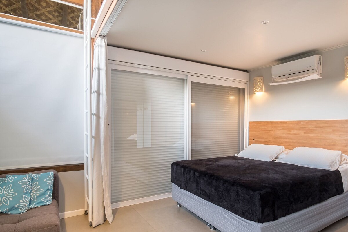 A bedroom with a bed, a nightstand, a window with blinds, an air conditioning unit, and a sliding door.