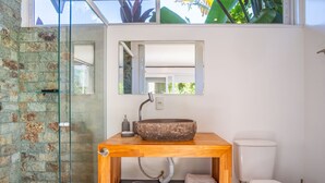 Un baño con lavamanos de piedra, tocador de madera, cabina de ducha de vidrio y un inodoro.