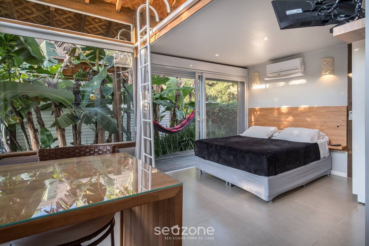 Un dormitorio moderno con una cama, mesita de noche y un ventanal grande con vistas a un jardín.