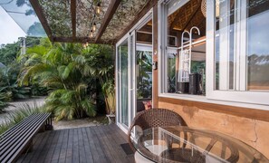 A wooden deck with a glass table and wicker chairs, surrounded by lush greenery. - VGZ Cabanas Barra de Ibiraquera e Rosa (Imbituba)