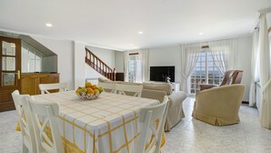 Un área de comedor con una mesa dispuesta para cuatro, un sofá, un televisor y una escalera.