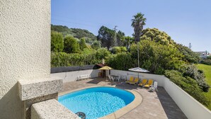 Una piscina de borde curvo, rodeada por un patio con sillas y una pequeña mesa.