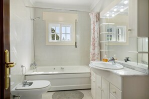 Un bagno con servizi igienici, vasca e lavandino, con una finestra sopra la vasca e uno specchio sopra il lavandino.