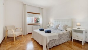 Un dormitorio con cama, mesitas de noche, una silla y un ventanal.