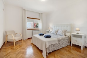 Um quarto com uma cama, mesas de cabeceira, uma cadeira e uma janela.