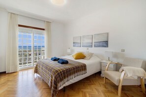 Una camera da letto con un letto, una sedia, un comodino e vista mare dalla finestra.