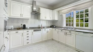 Una cocina con armarios blancos, extractor de acero inoxidable, lavavajillas y ventana con vistas al verdor.