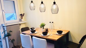 A dining area with a wooden table, white chairs, black bowls, wine glasses, a potted plant, and hanging pendant lights. - 2 bedrooms in the heart of city center (Luxembourg City)