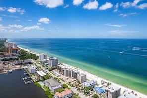An aerial view of a coastal city with a marina, beachfront hotels, and clear blue waters.