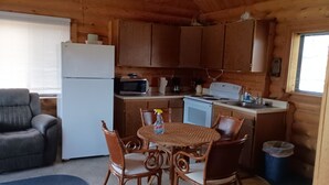 A compact wooden cabin with a kitchenette, a dining area with wicker chairs, and a gray sofa.