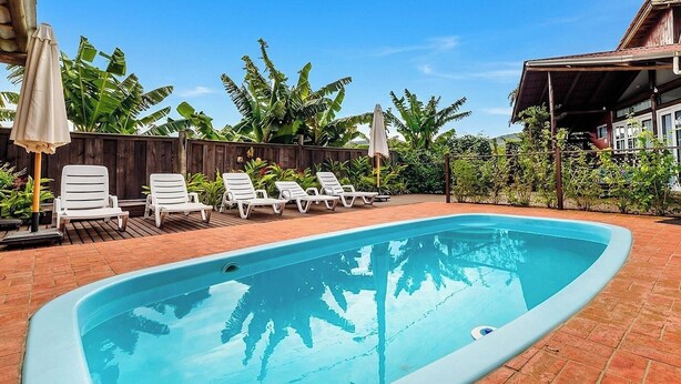 Una piscina rettangolare con bordo piastrellato, circondata da poltrone a sdraio bianche e ombrelloni.
