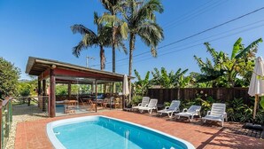 Una piscina con lettini, un'area relax coperta e alte palme.