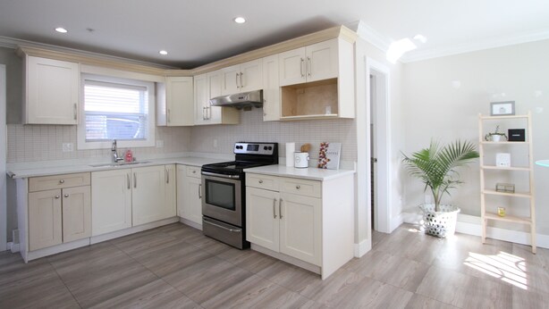 A modern kitchen with white cabinetry, a stainless steel oven, and a window with blinds. - Centrally located 2 bedroom 1.5 bathroom, 15 mins to DT Vancouver (Vancouver)