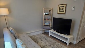 A living room with a sofa, a flat-screen TV on a stand, a floor lamp, a bookshelf, and a patterned rug. - Centrally located 2 bedroom 1.5 bathroom, 15 mins to DT Vancouver (Vancouver)