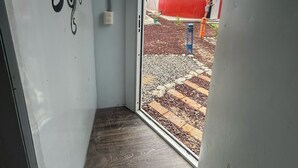 A narrow hallway with a wooden floor leading to a glass door. A black octopus design is on the wall, and a red spherical structure is visible outside. - Casa Faro 5 minutes from the beach  (Barra de Navidad)