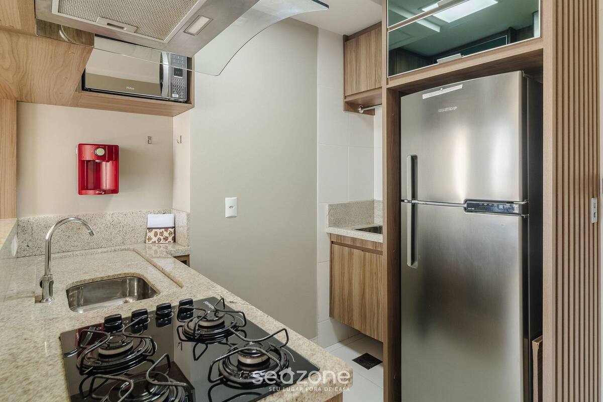 A modern kitchen with a stainless steel refrigerator, a gas stove, a microwave, and a red water dispenser.