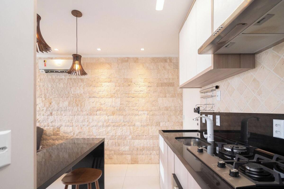 A modern kitchen with a stone backsplash, stainless steel appliances, and a hanging pendant light.
