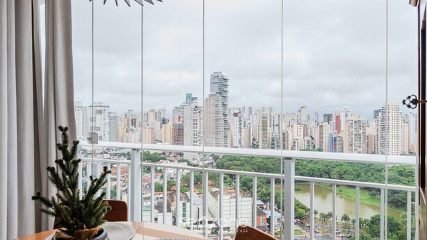A balcony with a city view, a potted plant, and a table. - WBU - Studios Modernos no Setor Bueno (Goiânia)
