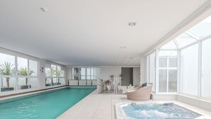 An indoor swimming pool with a hot tub, large windows, and wicker furniture. - WBU - Studios Modernos no Setor Bueno (Goiânia)