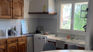 Een moderne keuken met houten kastjes, een wit aanrecht, een witte eettafel met stoelen, en een raam dat natuurlijk licht binnenlaat.