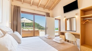 Habitación de hotel con cama, una silla, televisión, armario y balcón con vistas a zonas verdes.