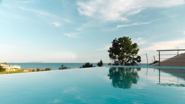 Una piscina con vistas despejadas al mar y un árbol al fondo.
