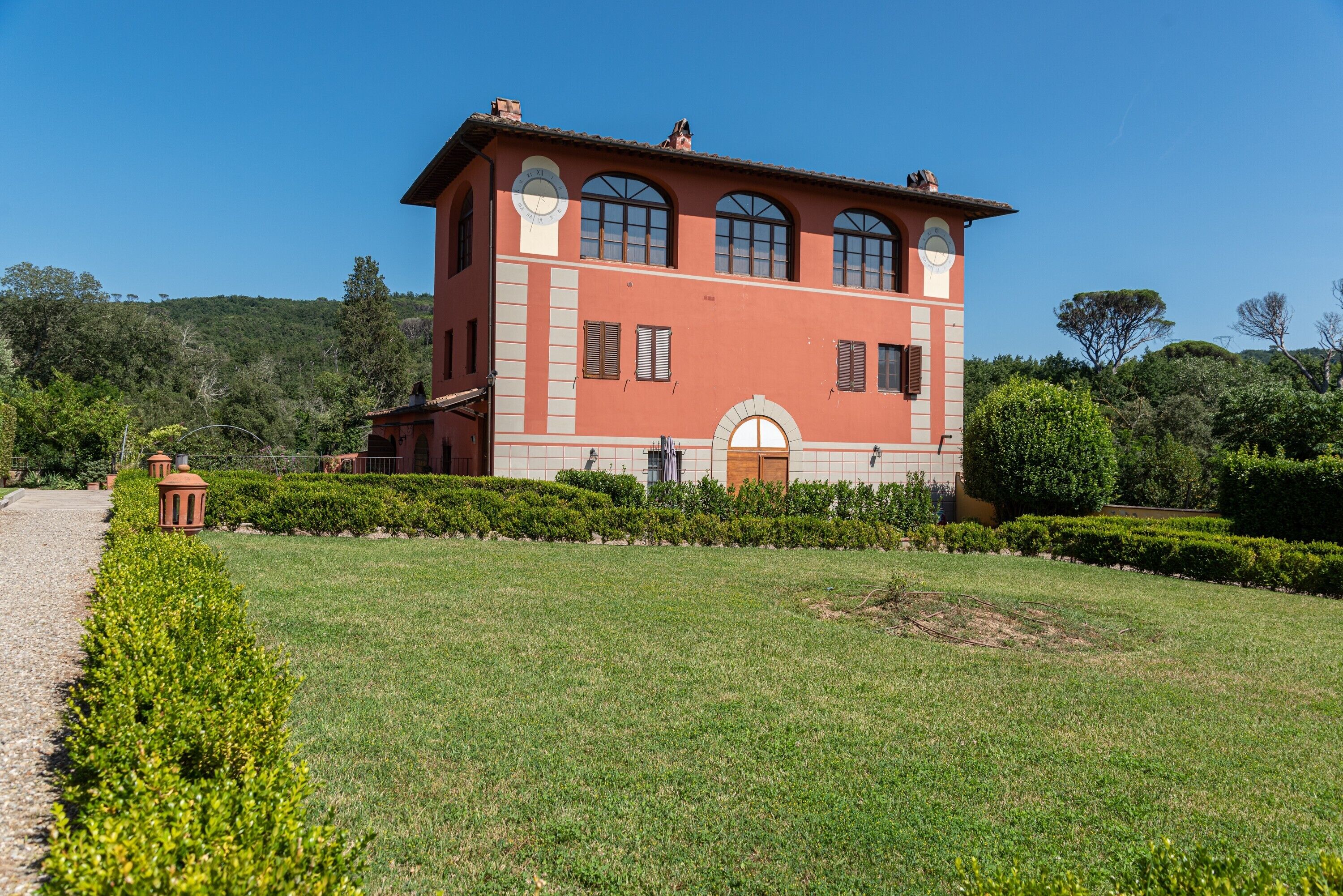 Un bâtiment à deux étages, surmonté d’une tour horlogée, entouré d’un jardin bien entretenu et baigné par un ciel dégagé.