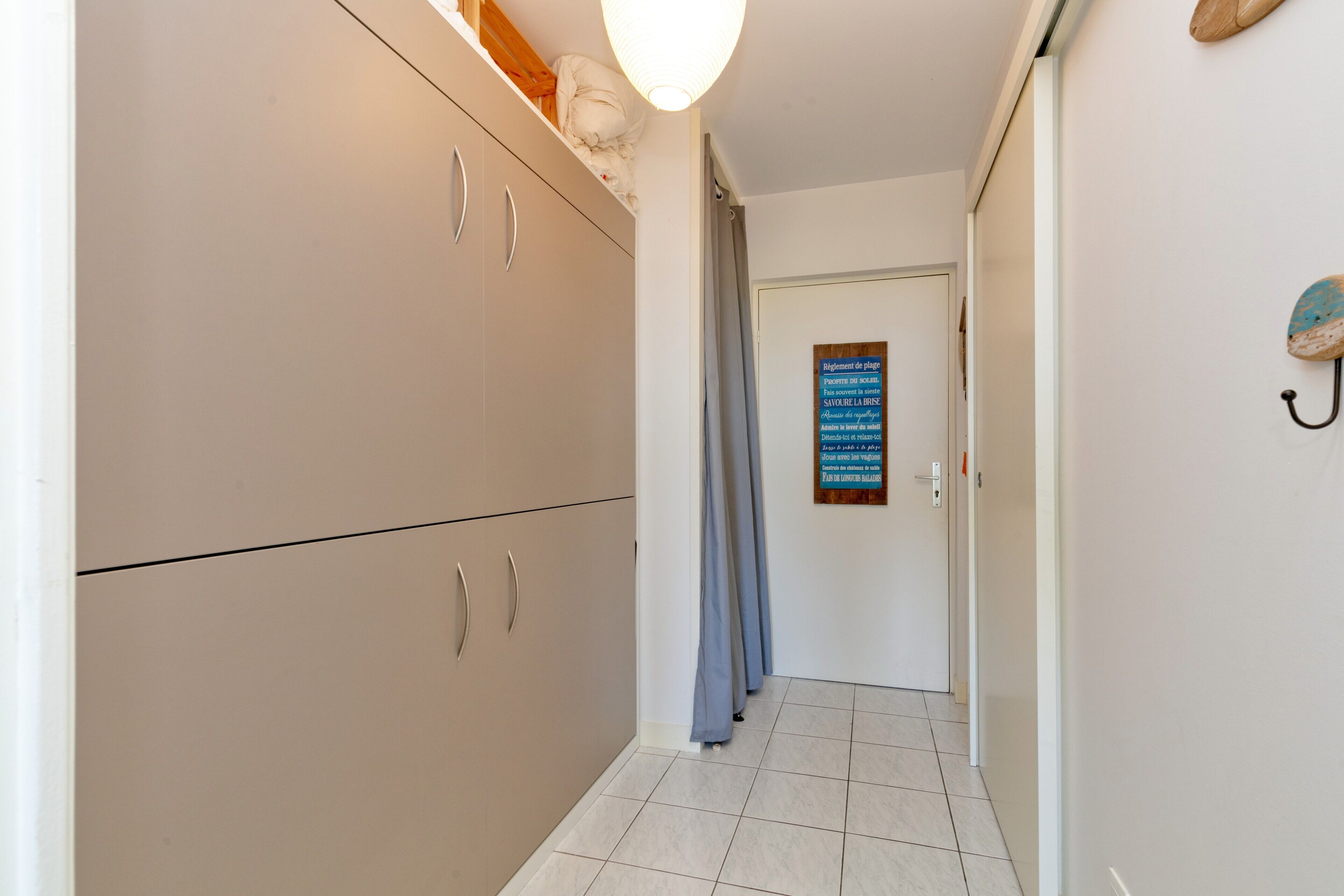 A hallway with a wardrobe, a door with a sign, and a hook on the wall.
