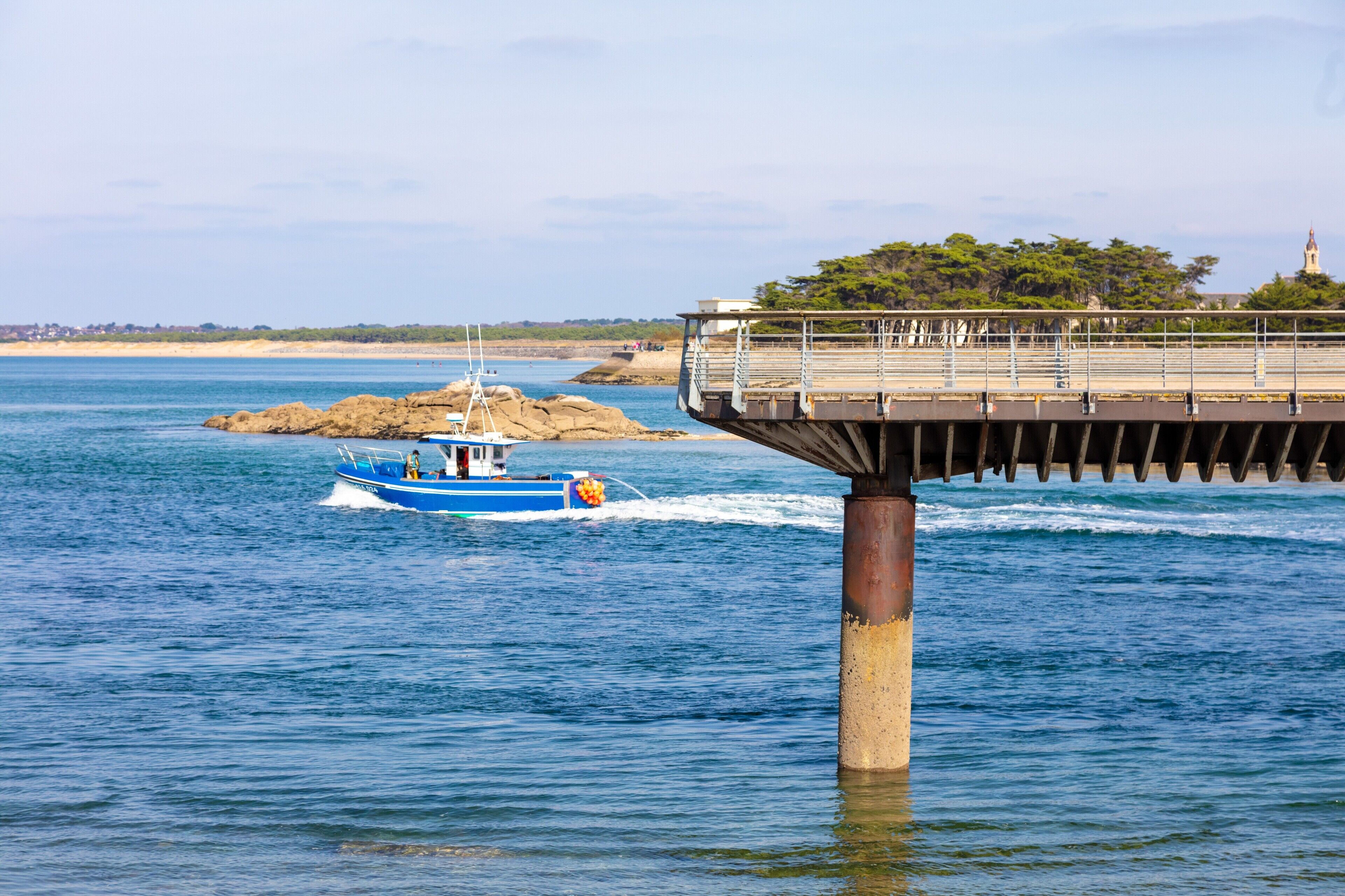 Une jetée qui s’avance dans une étendue d’eau, avec un bateau qui passe en dessous.