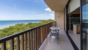 A balcony with a table and chairs, overlooking a beach and ocean.