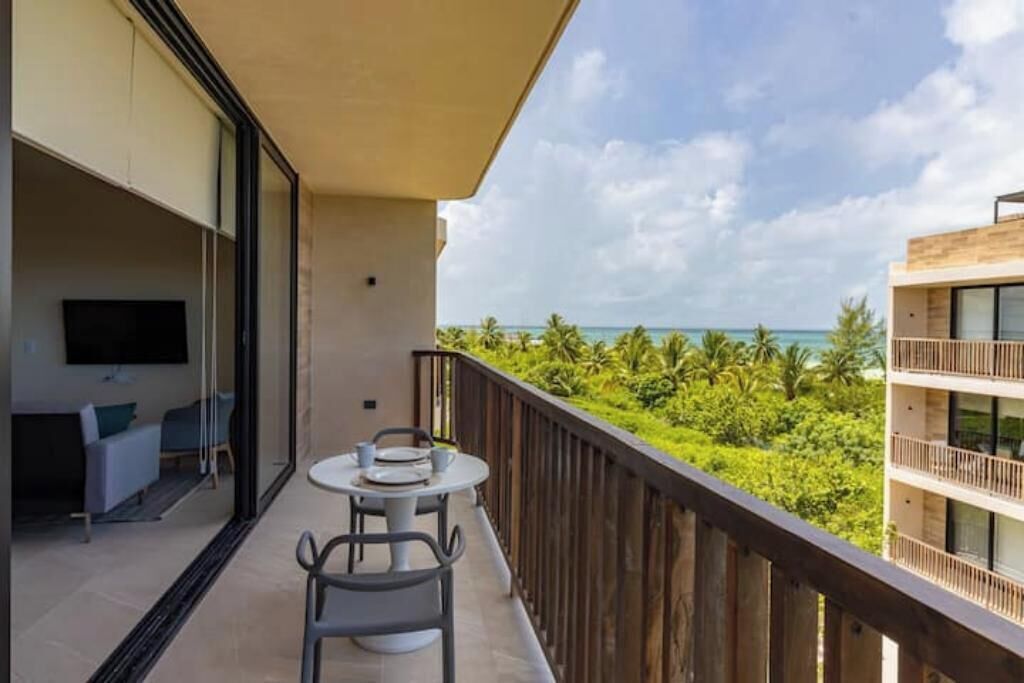 A balcony with a table and chairs, overlooking a lush green landscape and the sea.