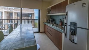 A kitchen with a dining area, a refrigerator, and a view of a building with balconies.