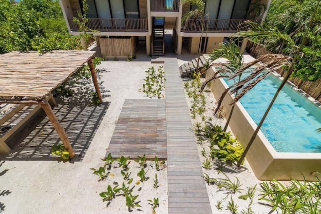 A poolside area with a wooden deck, a small pool, and surrounding greenery.