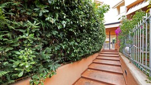 A staircase with a green hedge on one side and a metal fence on the other, leading to a building entrance. - 'Loano Relax' Apartment with Private Terrace and Garden (Loano)
