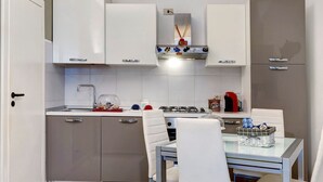 A compact kitchen with a dining area, featuring a stainless steel sink, a gas stove, and white cabinetry. - 'Loano Relax' Apartment with Private Terrace and Garden (Loano)