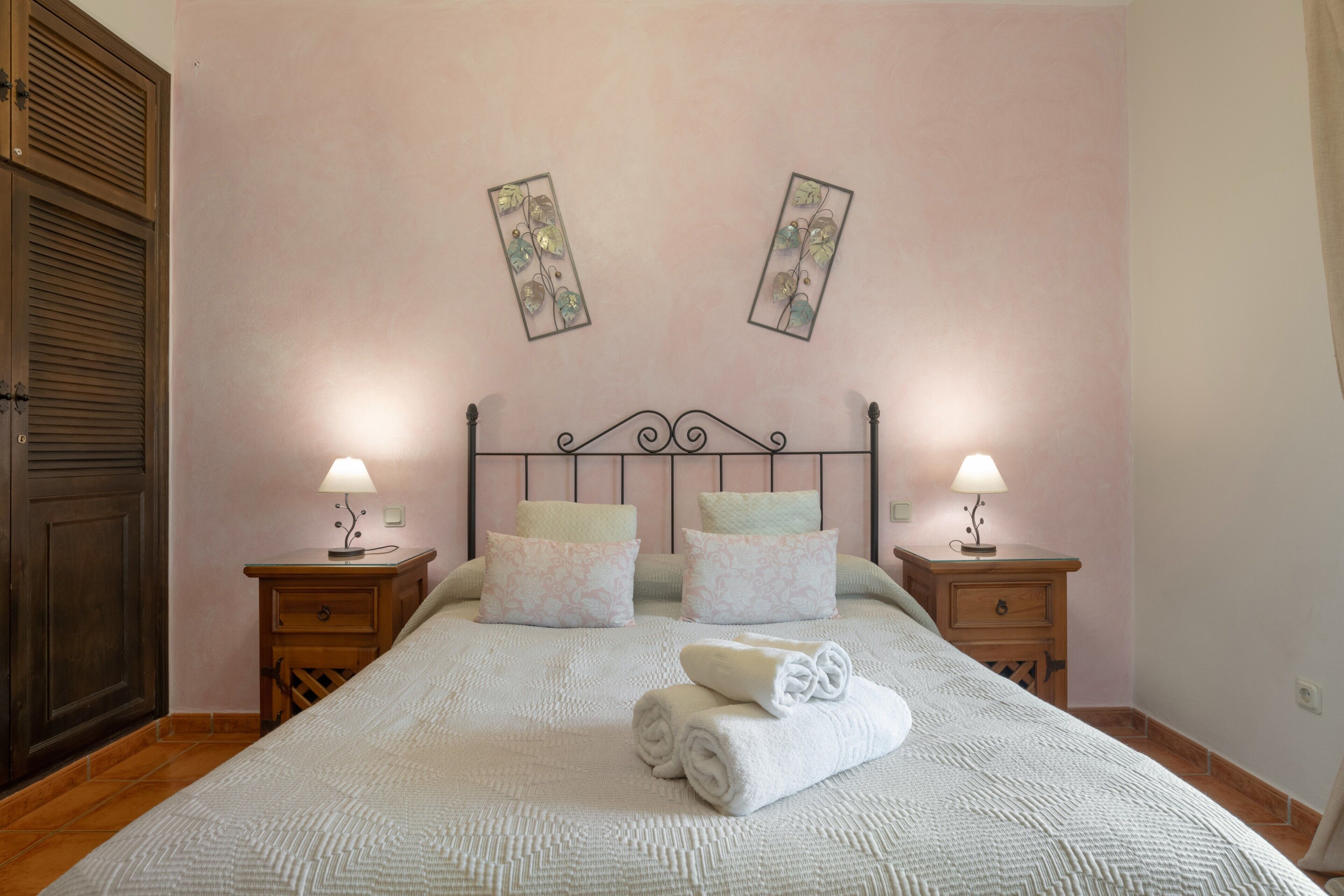 A neatly made bed with pillows, a folded towel, and two bedside tables with lamps.
