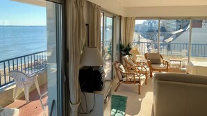 Een balkon met uitzicht op de zee, ingericht met rieten stoelen en een bank, en een lamp op een bijzettafeltje.