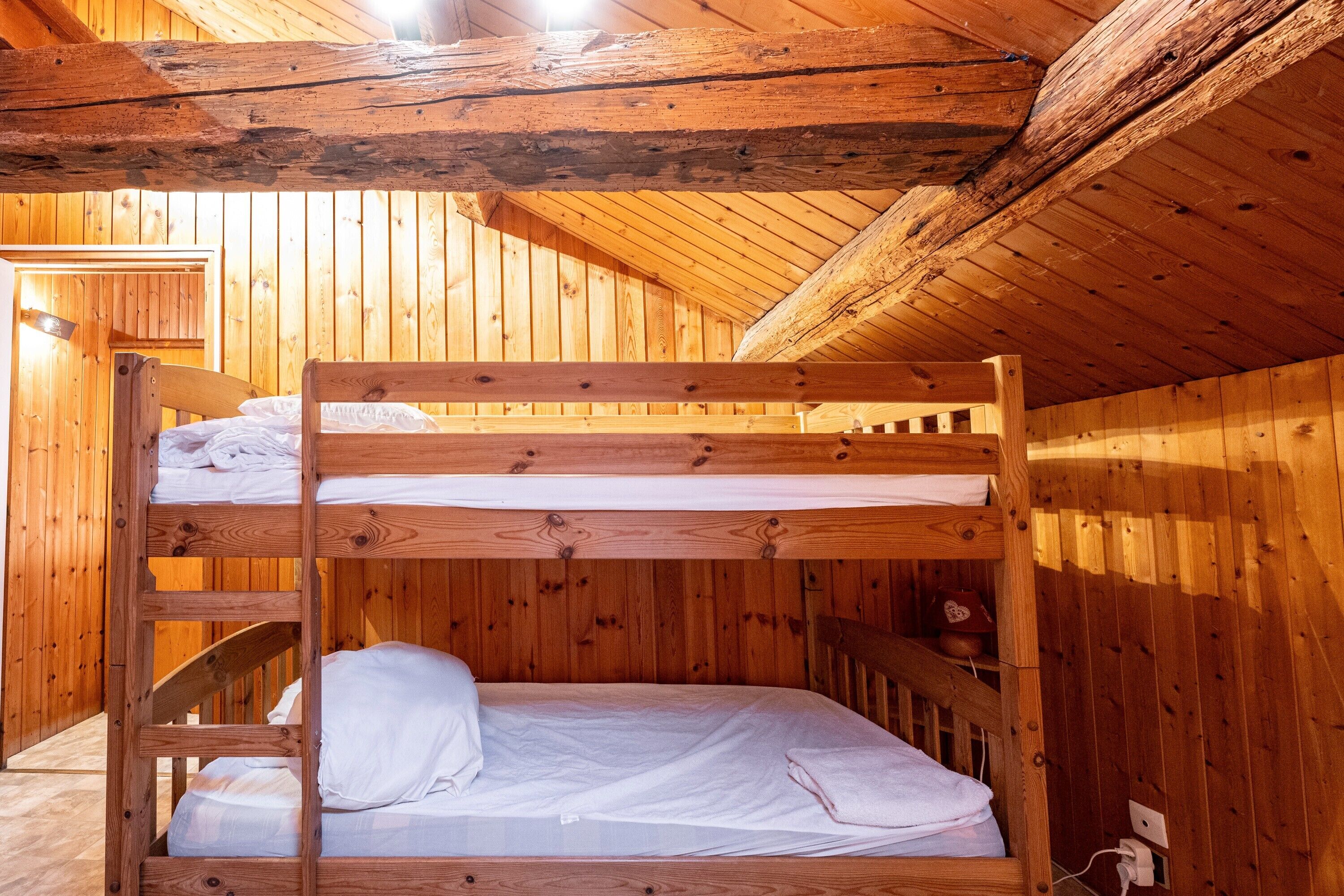 Een slaapkamer met stapelbedden, houten wanden en plafond, een houten trap en een klein plankje met een rood voorwerp.