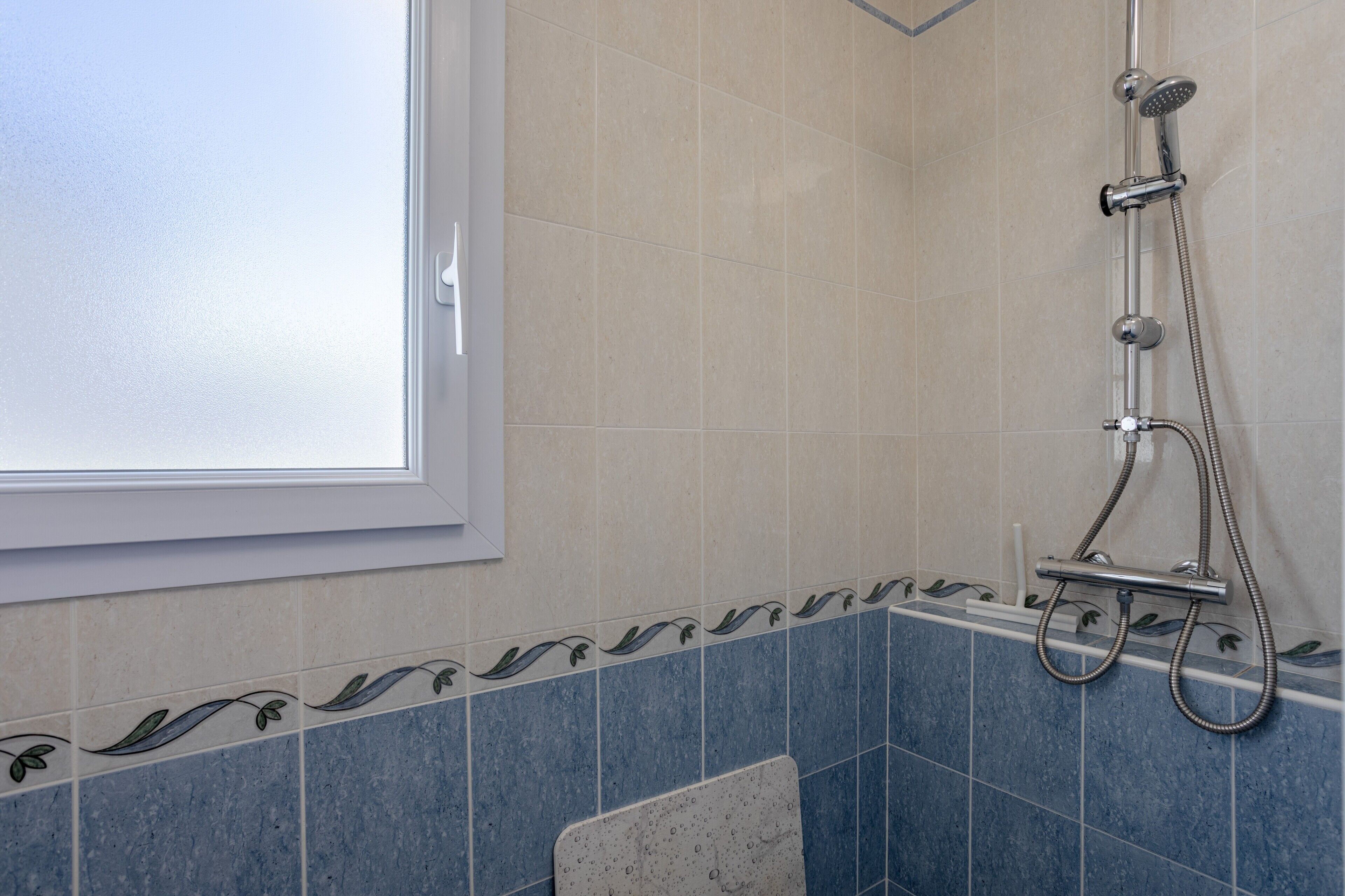 A bathroom with a shower, a window, and decorative tiles.