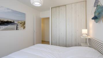 Ein Schlafzimmer mit einem großen Bett, einem Holzschrank, einer Wandleuchte und einem Gemälde zum Thema Strand.