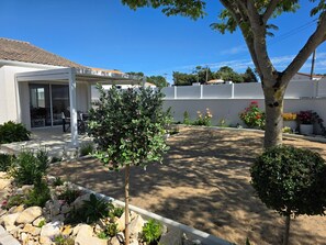 Ein Wohnhaus mit überdachter Terrasse, einem kleinen Baum, einem Felsengarten und einer weißen Mauer.