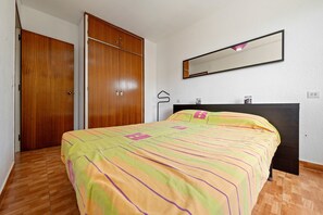 A bedroom with a bed, wooden wardrobe, and a mirror on the wall.