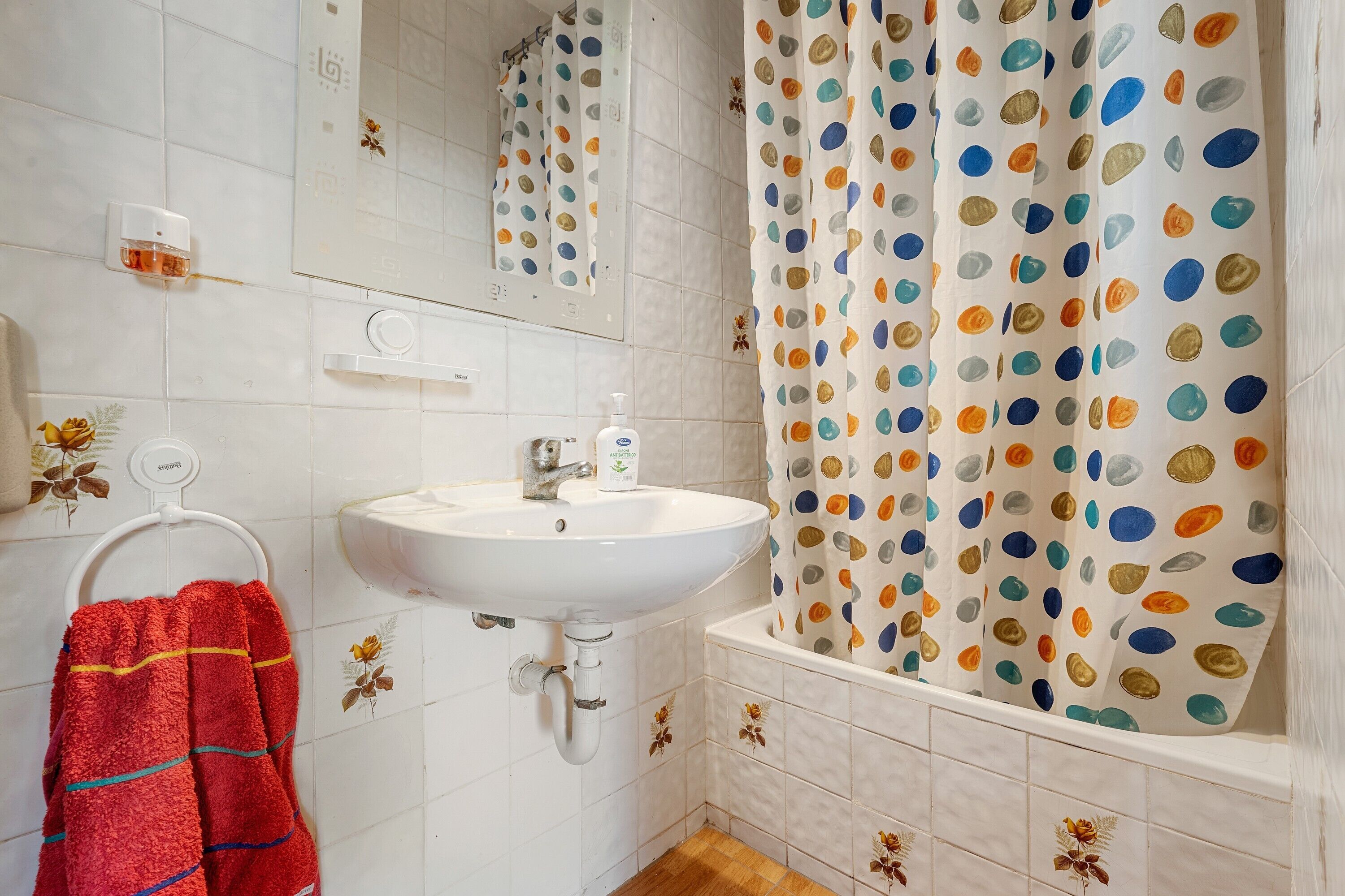 A bathroom with a white sink, a mirror, a towel rack, and a shower curtain with a polka dot pattern.